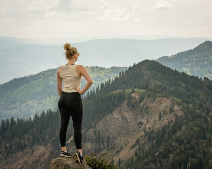 Photo by Brandon Zacharias a man standing on a rock overlooking a valley with trees and mountains